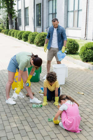 Family in rubber gloves sorting garbage near cans on urban streetの写真素材