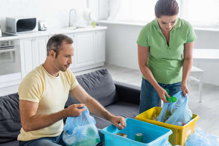 Adult couple with trash bags and boxes sorting garbage in kitchen
