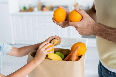 Cropped view of father and son holding fruits near paper bag at homeの写真素材