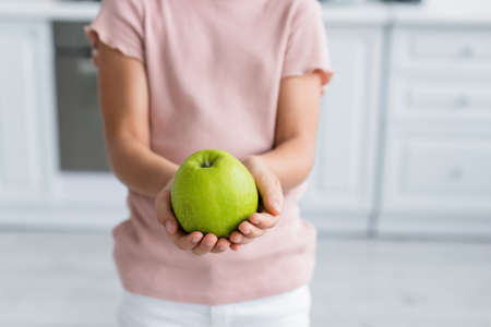 Cropped view of green apple in hands of blurred kidの写真素材