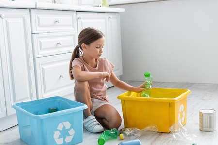 Girl sorting bottles in boxes with recycle sign in kitchen