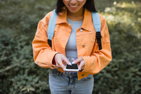 cropped view of smiling woman in orange jacket using cellphone with blank screenの写真素材