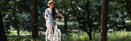 young asian woman in sundress and straw hat riding bicycle in park, bannerの写真素材