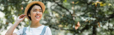 happy asian woman in straw hat looking away outdoors, bannerの写真素材