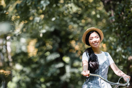 happy asian woman in straw hat smiling at camera while biking in parkの写真素材