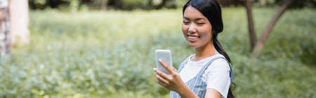 joyful asian woman chatting on mobile phone in park, bannerの写真素材