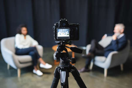 digital camera with african american journalist talking with businessman during talk show on screen