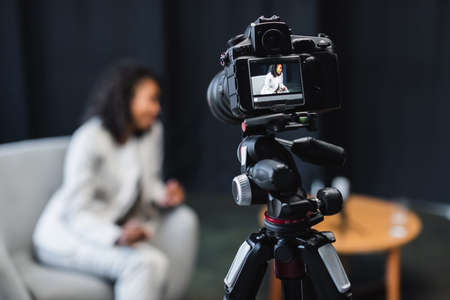 modern digital camera on tripod with african american journalist sitting in armchair on screenの写真素材