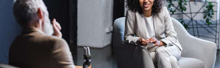 cropped view of happy african american journalist talking with blurred businessman during interview,...
