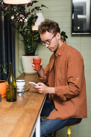 young man in glasses texting on smartphone in cafe