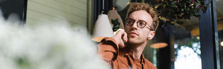 low angle view of young man in glasses adjusting wireless earphones in cafe, bannerの写真素材
