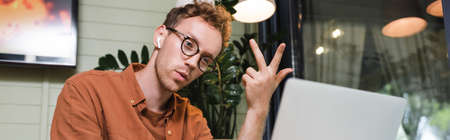 man in glasses and wireless earphones having video call on laptop, banner