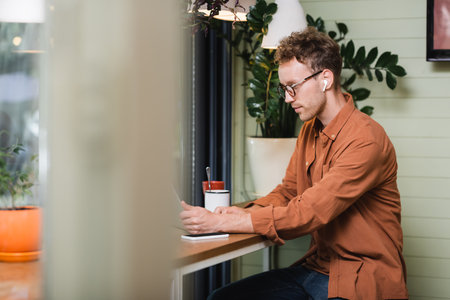 freelancer in glasses looking at laptop near smartphone in cafe