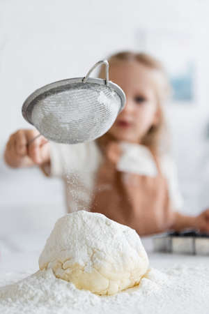close up view of sieve in hand of blurred girl sifting flour