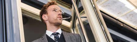low angle view of curly businessman in glasses and classy suit opening door while leaving cafe, bannerの写真素材