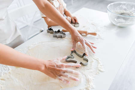 cropped view of woman cutting dough with cookie cutter near daughter in kitchenの写真素材