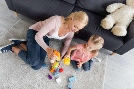 overhead view of mother and daughter playing with building blocks on floor at homeの写真素材