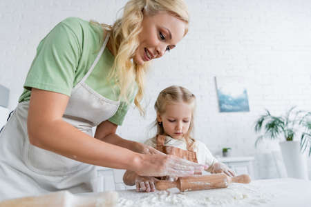 girl rolling dough near smiling mom in kitchenの写真素材