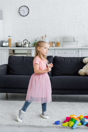 girl in toy crown and tulle skirt standing with magic wand at homeの写真素材