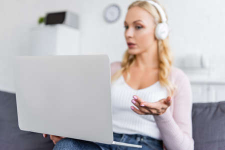 blurred woman in headphones pointing with hand at computer during video call