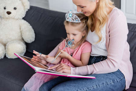 mom and daughter pointing at book while reading fairy tale on couch at homeの写真素材