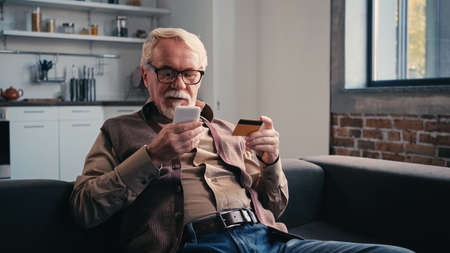 pensioner with credit card holding mobile phone while shopping online at homeの写真素材
