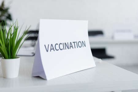 sign plate with vaccination lettering near green potted plant on desk in hospitalの写真素材