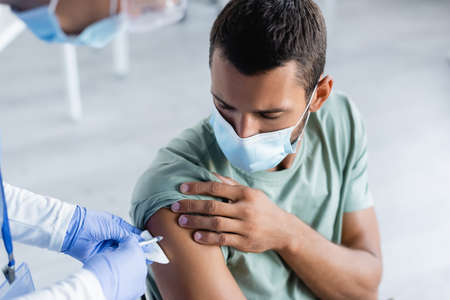 blurred nurse giving injection of vaccine to young man in protective maskの写真素材