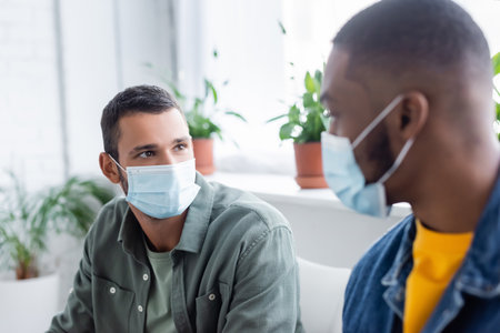multiethnic men in medical masks talking in hospital, vaccination conceptの写真素材