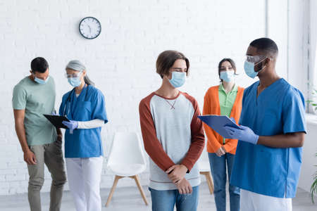 interracial physicians writing on clipboards while talking to patients in vaccination centerの写真素材