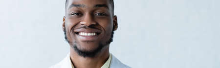 young and happy african american doctor smiling at camera on white background, banner