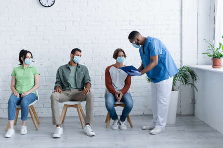 african american man standing with clipboard near patients, vaccination concept