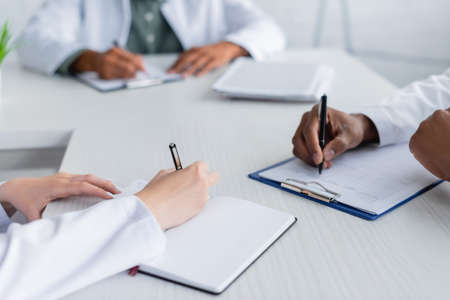 cropped view of multiethnic doctors writing during council in meeting roomの写真素材