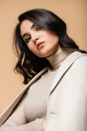 young pretty model in turtleneck and blazer looking at camera isolated on beigeの写真素材