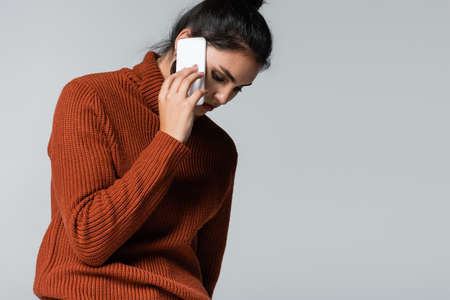young woman in knitted sweater talking on mobile phone isolated on greyの写真素材