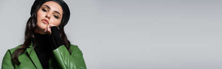young model in black turtleneck, green jacket and beret looking at camera isolated on grey, bannerの写真素材