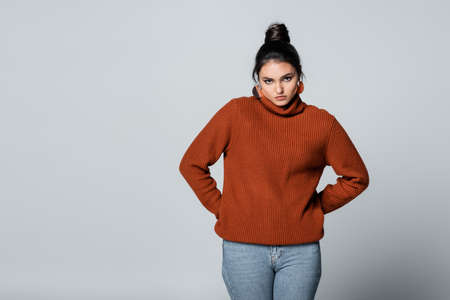 young woman in sweater and denim jeans posing with hands on hips isolated on greyの写真素材