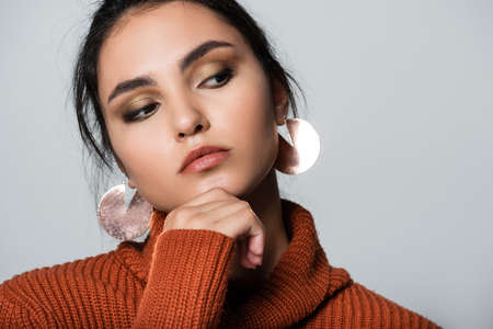 young woman in warm sweater and earrings looking away isolated on greyの写真素材