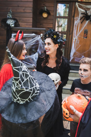 happy mom and daughter smiling at each other near family in halloween costumesの写真素材