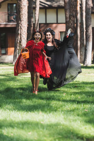 excited woman and girl in halloween costumes screaming while running in backyardの写真素材