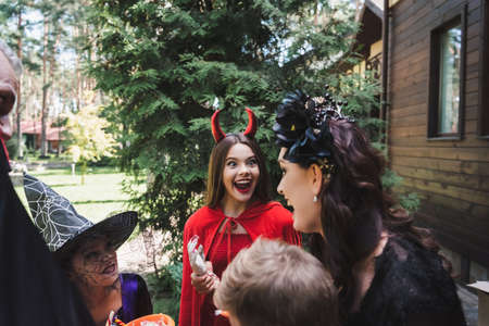 excited girl in devil halloween costume near family outdoorsの写真素材