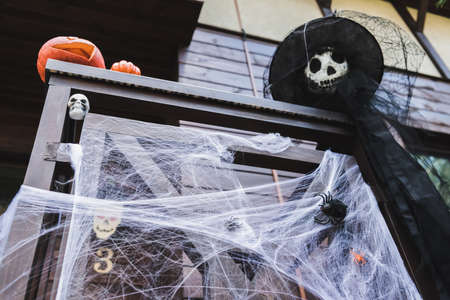 low angle view of carved pumpkins and scarecrow in witch hat on porch fence decorated with spider netの写真素材