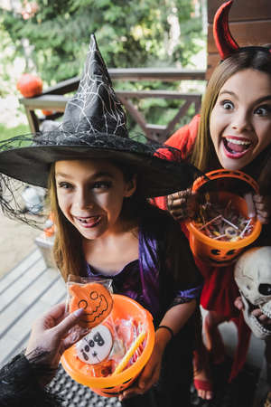 amazed sisters in witch and devil costumes near mother with halloween cookieの写真素材