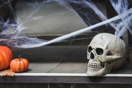 creepy skull and orange pumpkins near blurred spider net on house porchの写真素材