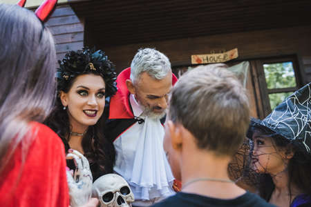 spooky woman in halloween costume holding skull and grimacing near family