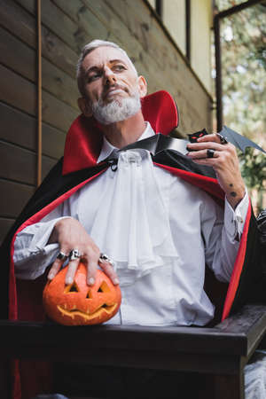 mature man in vampire halloween costume, with paper cut bat and curved pumpkinの写真素材