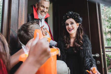 cheerful couple in scary halloween costumes near blurred kids on cottage porchの写真素材