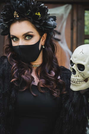 woman in halloween costume and black medical mask holding spooky skull while looking at cameraの写真素材