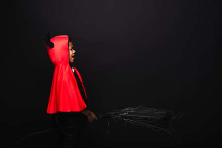 side view of scary african american kid holding broom and screaming isolated on blackの写真素材