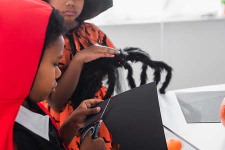 african american kid cutting black carton with bat template near blurred sister holding toy spiderの写真素材